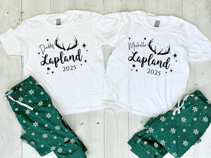 Lapland holiday matching pyjamas sets for family Lapland pyjama gift idea. Two white t-shirts with personalized text and green pajama pants on a wooden surface.