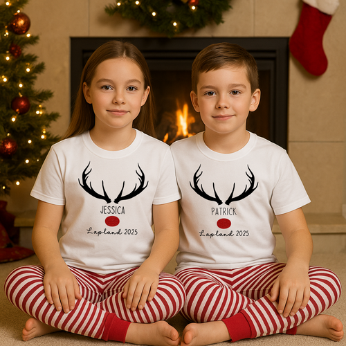Two children wearing matching pajamas with names and dates in front of a fireplace and Christmas tree. Family Lapland 2025 PJs set – matching family Lapland pyjamas for travel, personalised Lapland holiday PJs perfect for cosy Christmas celebrations and magical Lapland holiday matching outfits.