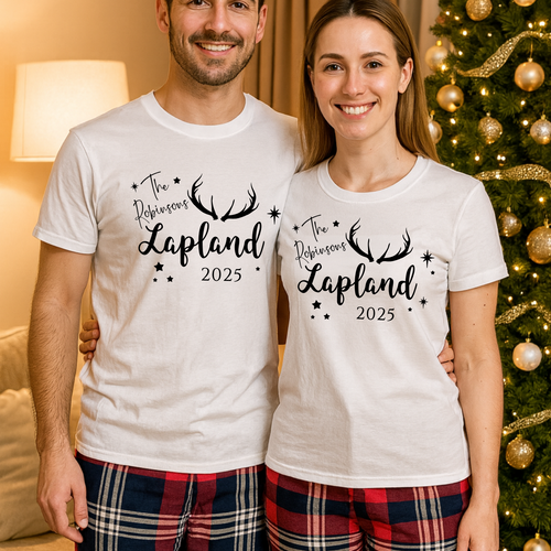 Two people wearing matching white t-shirts with 'The Reindeer's Lapland 2025' text, standing in front of a decorated Christmas tree.