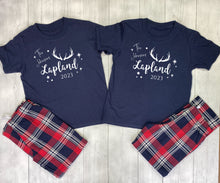 Load image into Gallery viewer, Two navy blue t-shirts with &#39;The Adventure is in Lapland 2023&#39; text and plaid shorts on a wooden surface.