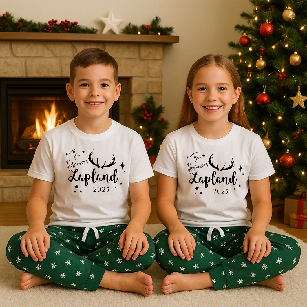 Personalised Lapland holiday PJs for Lapland trip reveal matching outfits.Two children wearing matching pajamas with 'Lapland 2025' text in front of a Christmas tree and fireplace.