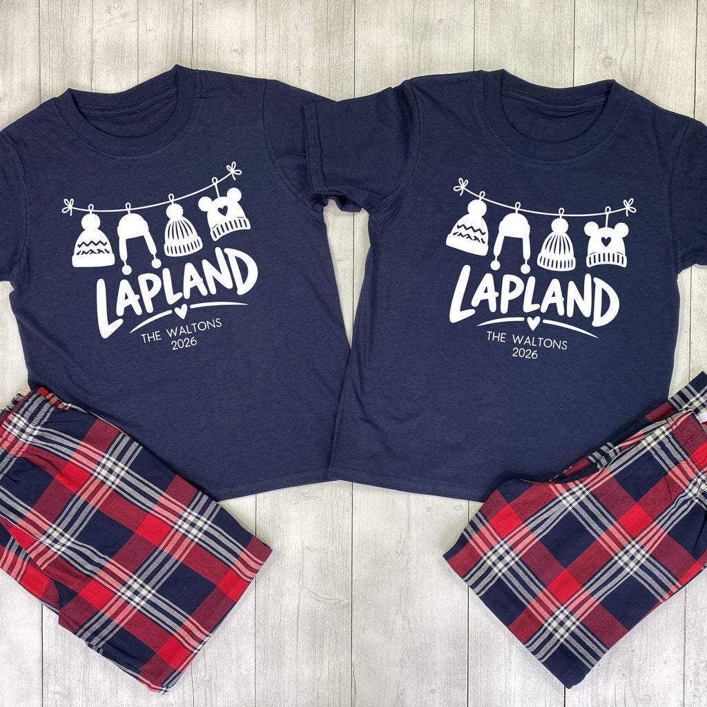 Matching Lapland pyjamas with navy T-shirts, white hanging bobble hats, The Waltons family name, 2026 and red and navy tartan bottoms.
