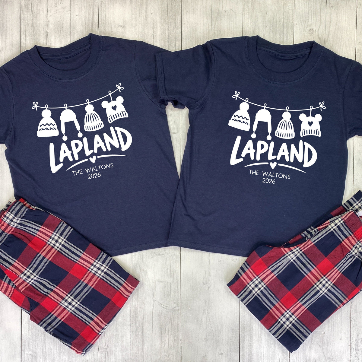 Matching Lapland pyjamas with navy T-shirts, white hanging bobble hats, The Waltons family name, 2026 and red and navy tartan bottoms.
