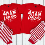 Two matching red pajama sets laid flat on a white wood plank background. Each set includes a short-sleeve shirt with a white graphic of knit hats hanging on a line above the text 'LAPLAND' and smaller text 'THE WALKERS 2026', paired with striped pants in red and white.