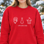 Woman wearing a red Lapland 2026 sweatshirt with white line illustrations of Santa, a Christmas tree and an elf in snowy woodland.