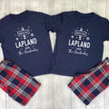 Two navy blue matching t-shirts with white graphic prints reading 'NORTH POLE 1 LAPLAND 2026 The Pembrokes' are laid flat on a light wood background, paired with red, navy, and white plaid shorts.